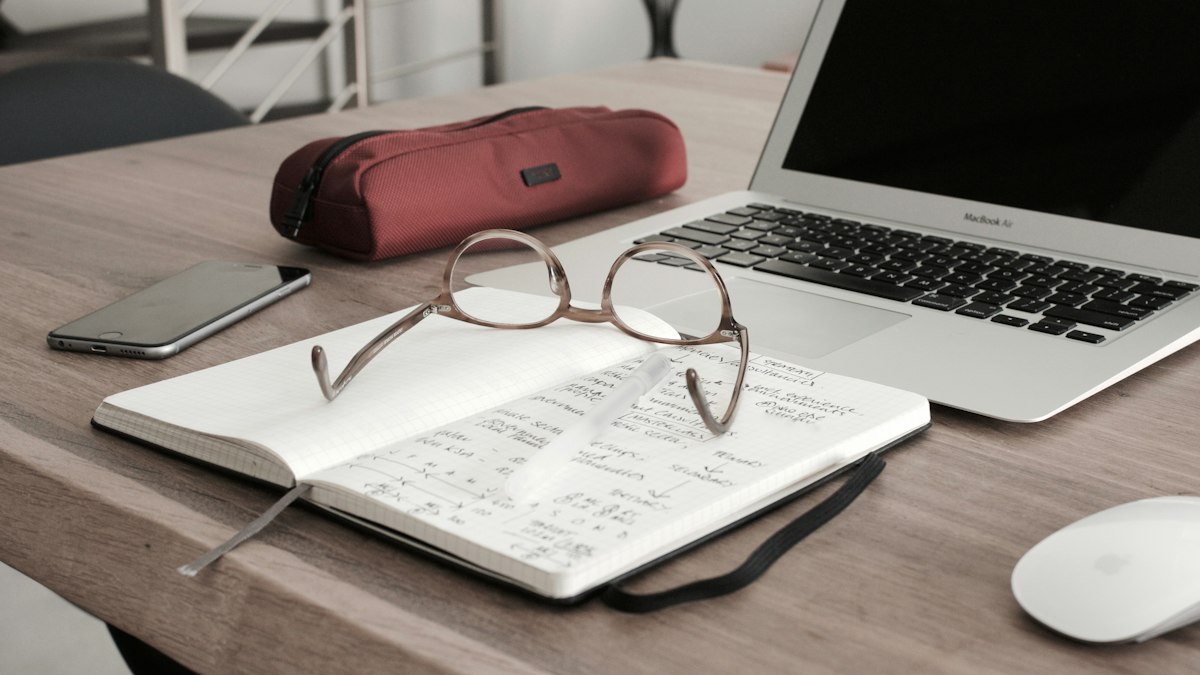 Brille auf einem Notizbuch neben dem Laptop am Arbeitsplatz